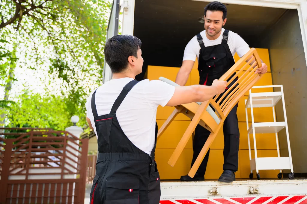 Two Delivery workers passing and carrying a chair