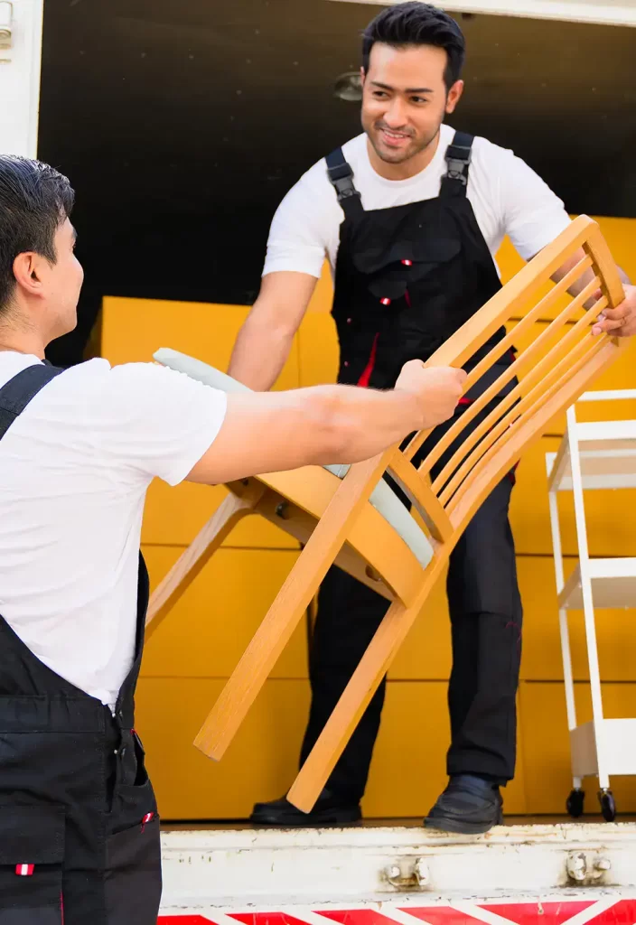 Two Delivery workers passing and carrying a chair